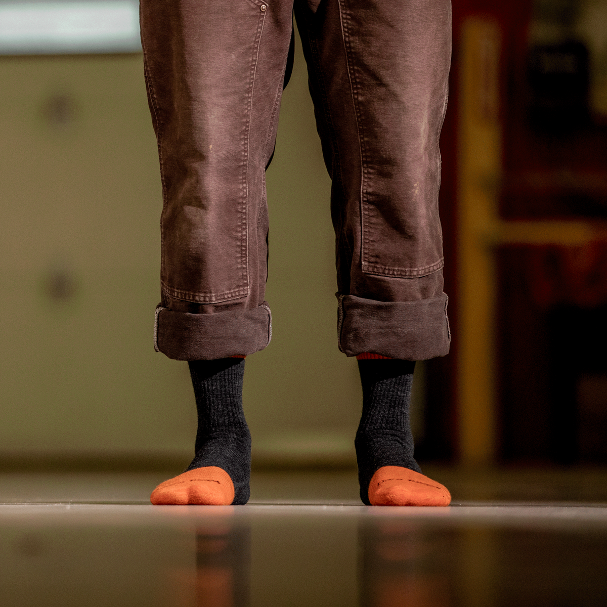Person wearing dark graphite crew socks with orange reinforced toe on reflective floor