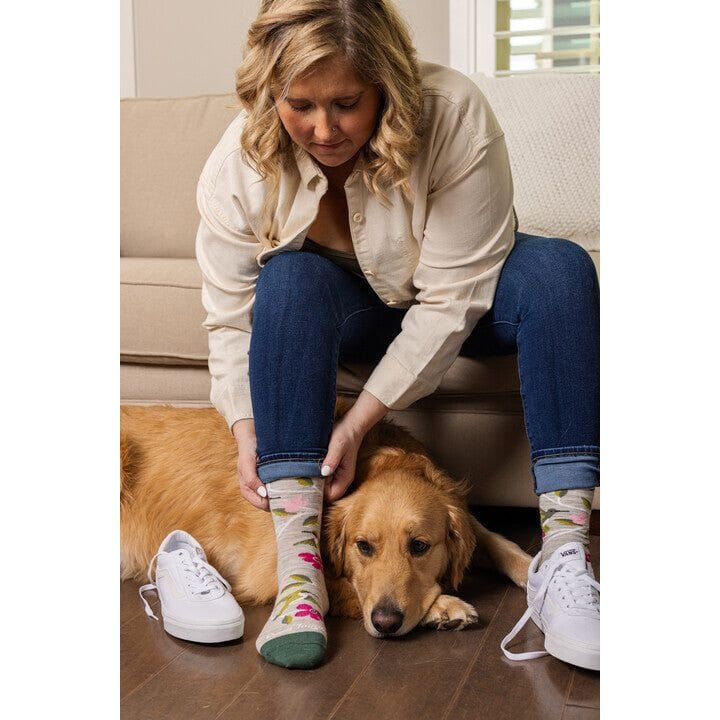 Woman sitting on couch showing floral crew socks beside a golden retriever dog