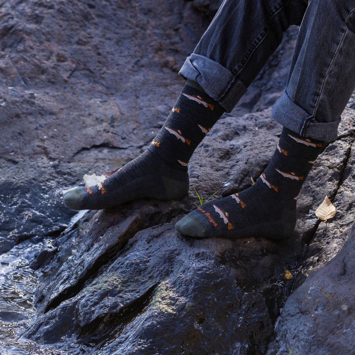 Person wearing dark crew socks with fish pattern standing on wet rocks near water