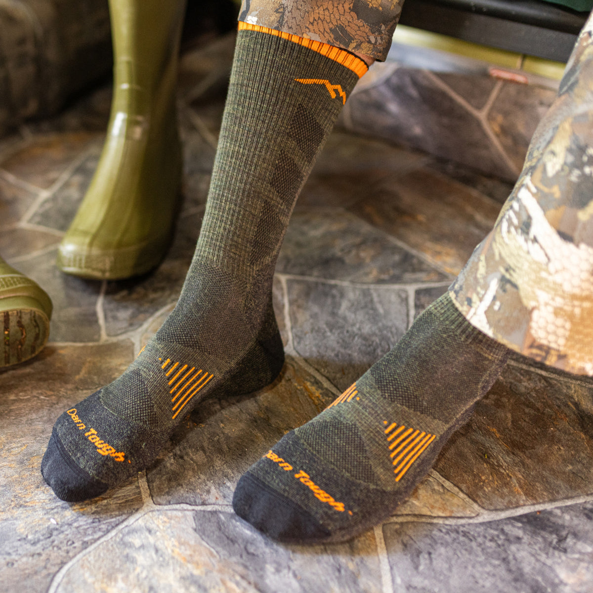 Darn Tough men's boot socks with orange accents worn standing on stone tile floor