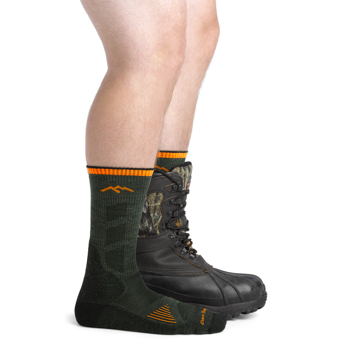Close-up of legs wearing dark green Darn Tough hunting socks with orange stripe detail paired with camo lace-up boots