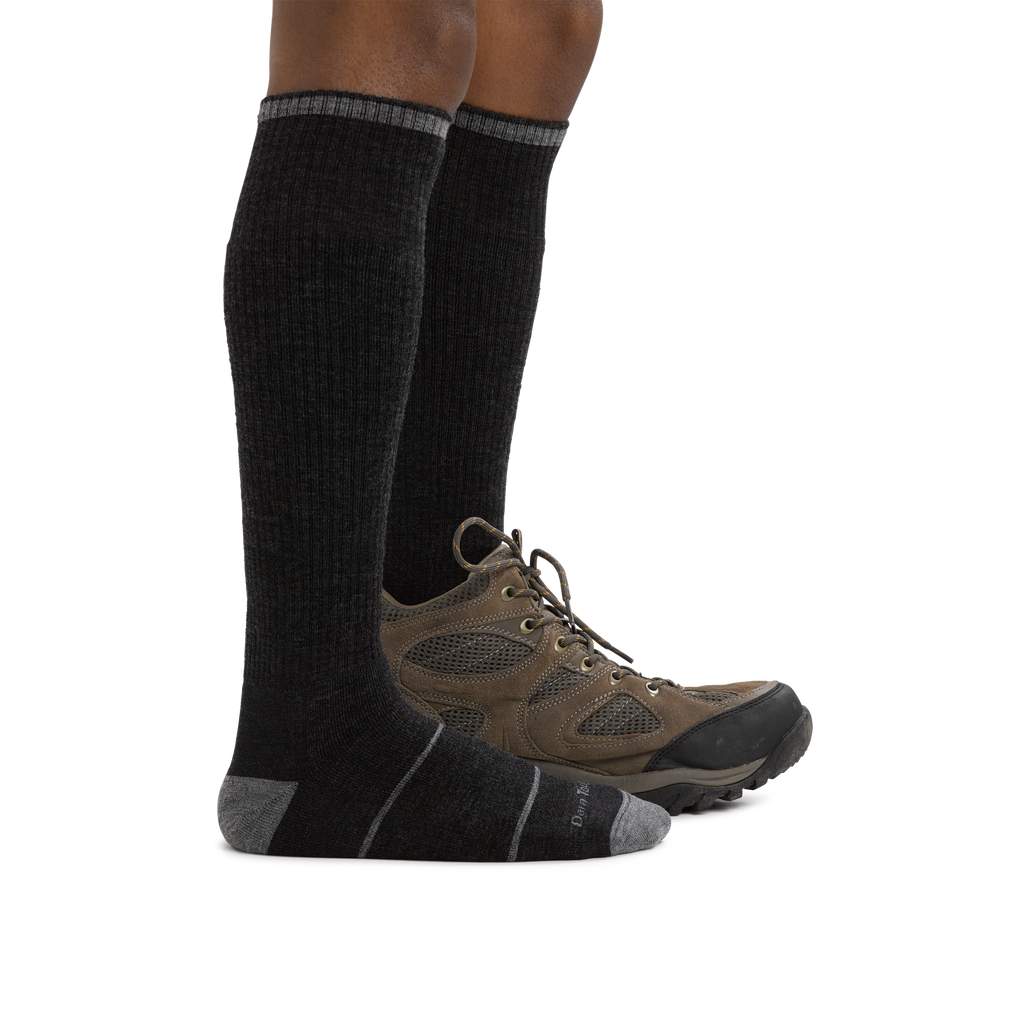 Model wearing tall black cushioned over-the-calf wool hiking socks with brown trail shoes