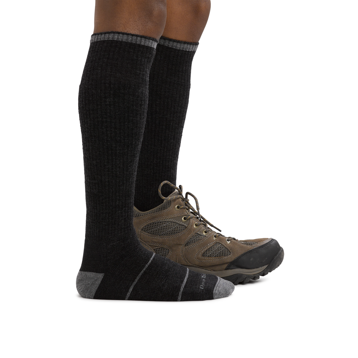 Model wearing tall black cushioned over-the-calf wool hiking socks with brown trail shoes
