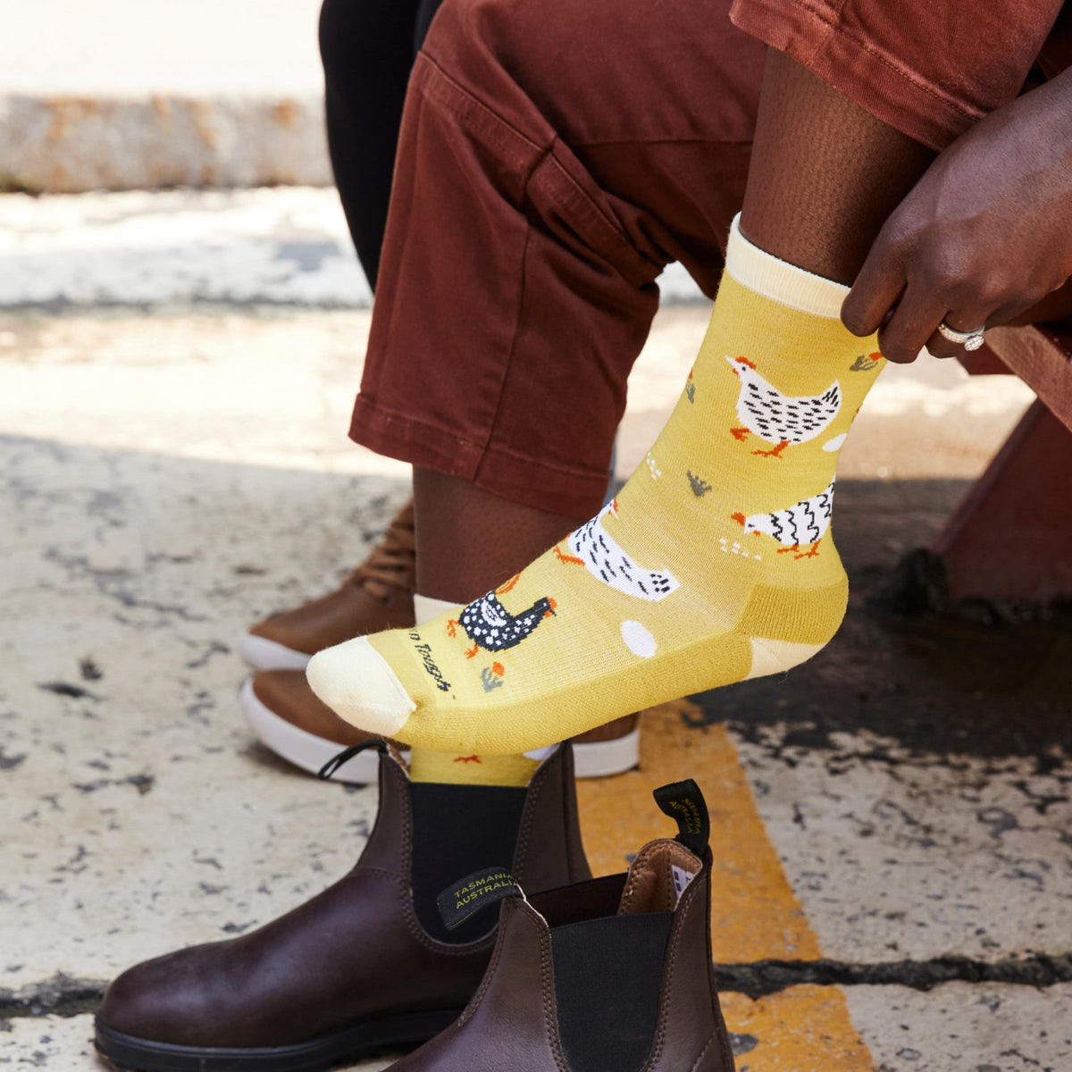 Person wearing yellow crew socks with chicken and egg pattern, paired with brown leather boots