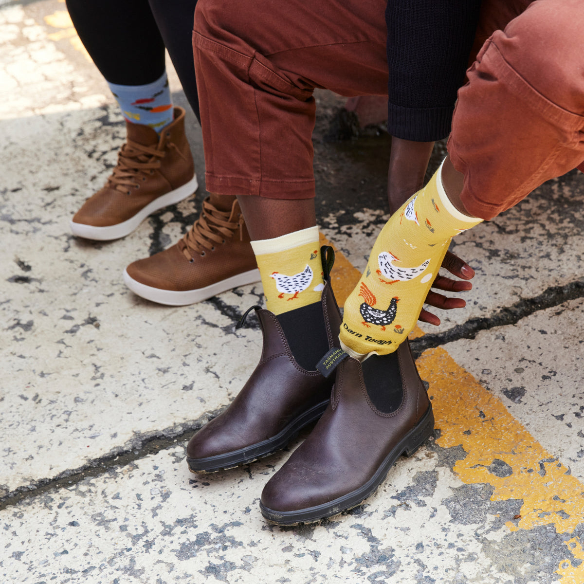 Model wearing yellow chicken-print crew socks with dark brown Chelsea boots outdoors