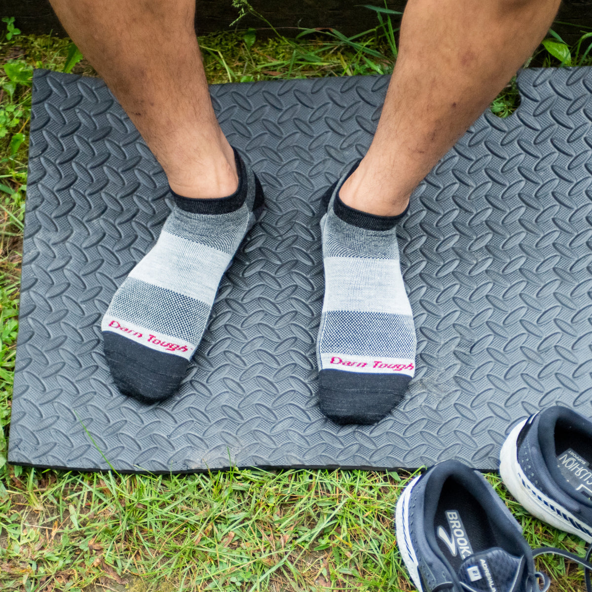 Person wearing Darn Tough no-show ankle socks standing on textured rubber mat outdoors