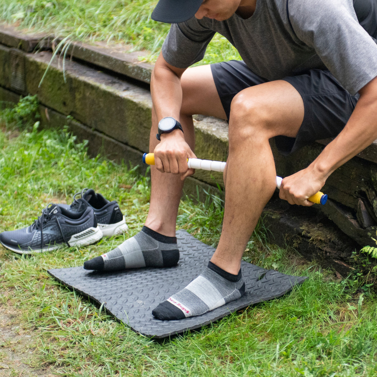 Man using sock aid tool to put on no-show running socks while seated outdoors on mat