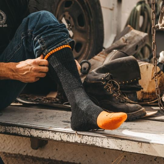 Darn Tough charcoal boot sock with orange toe being pulled on over work boots