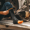 Darn Tough charcoal boot sock with orange toe being pulled on over work boots