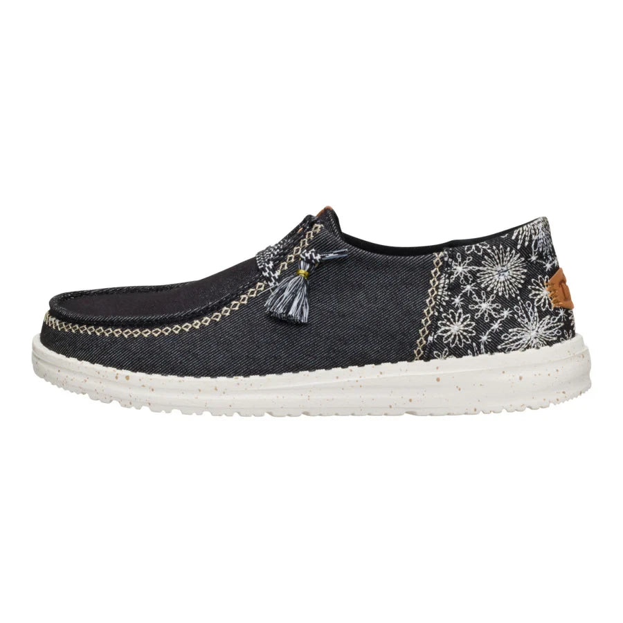 Hey Dude Wendy slip-on shoe in black denim with embroidered floral pattern and tassel detail