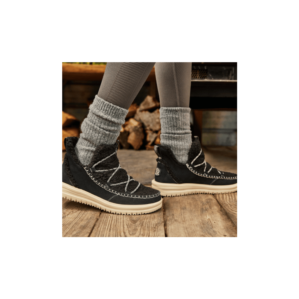 Women wearing black sherpa lace-up ankle boots with gray wool socks on wooden deck
