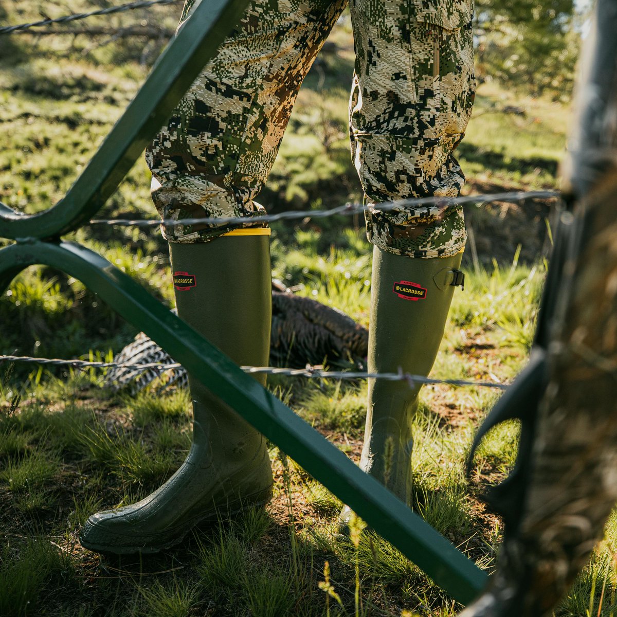 Person wearing LaCrosse tall rubber boots stepping through barbed wire fence in field