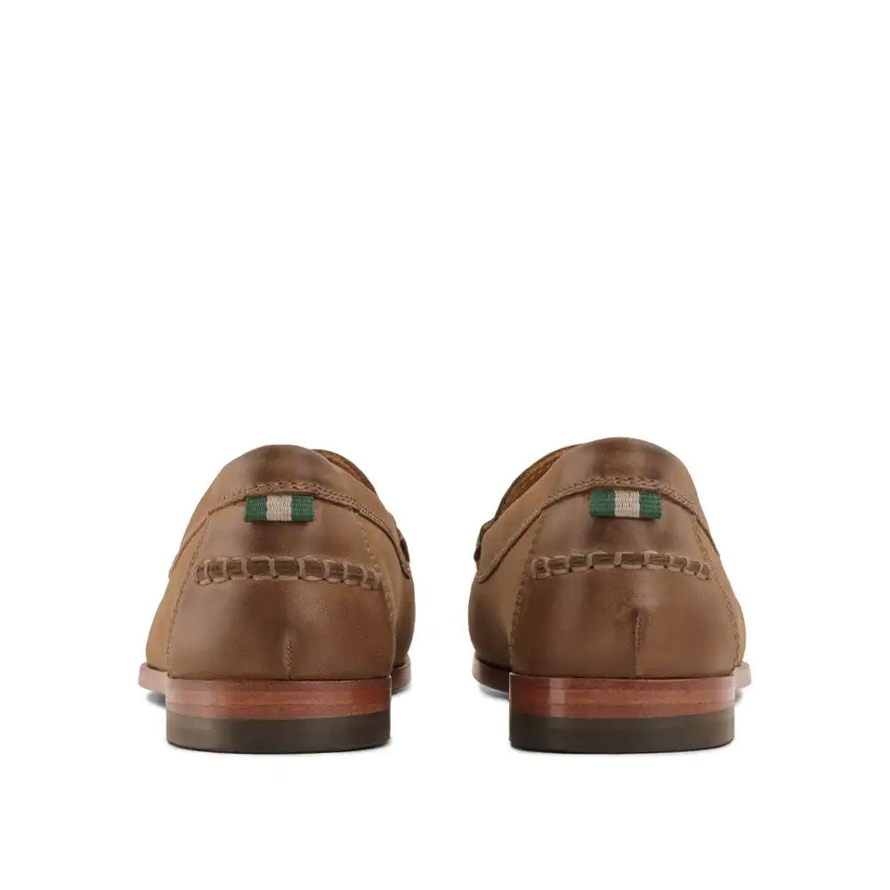 Back view of a pair of tan leather loafers with green and white striped heel tab and hand stitching