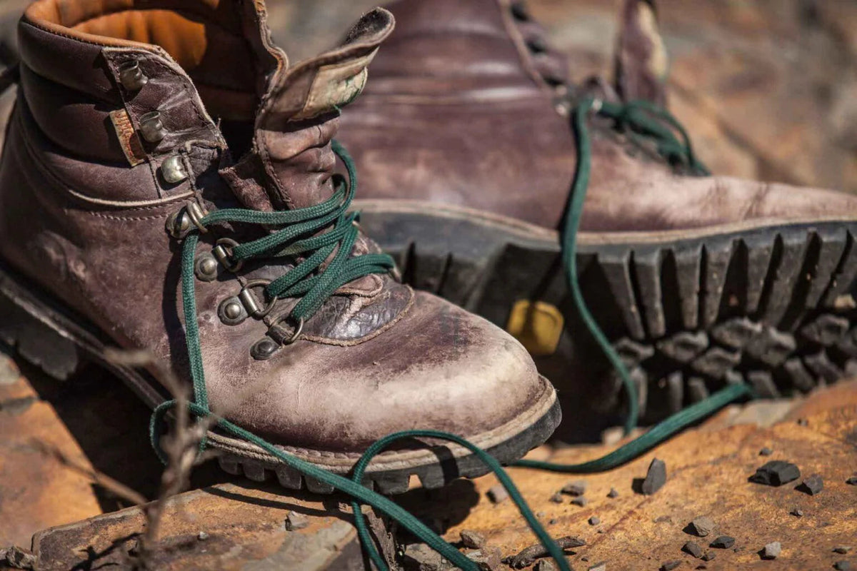 Worn russet leather hiking boots with green laces resting on rocky outdoor surface
