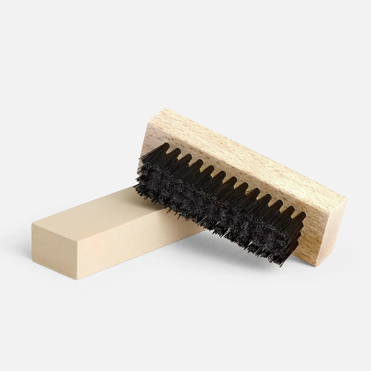 Wooden suede cleaning brush with dark bristles resting on a crepe eraser block