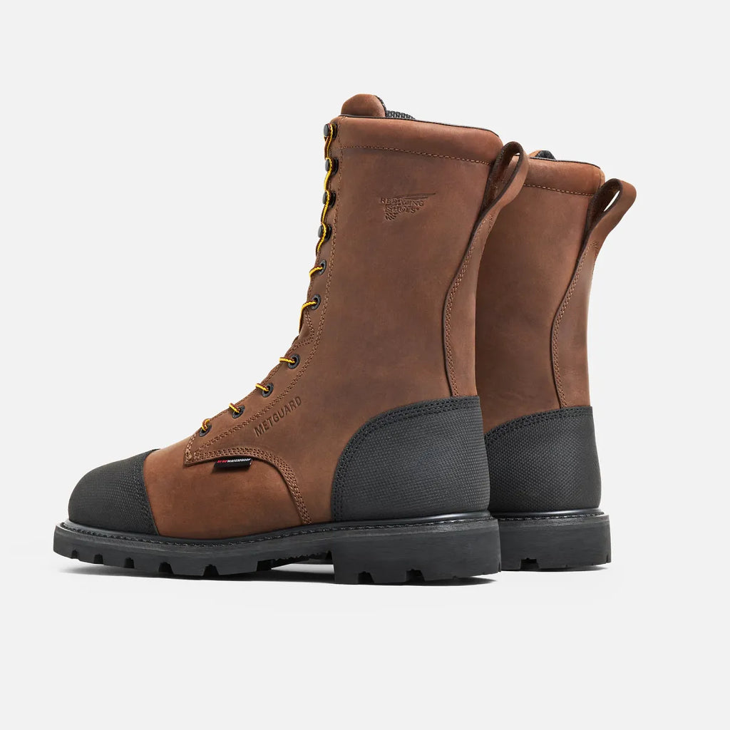 Red Wing steel toe metguard work boots with yellow laces and black rubber toe cap, angled rear view