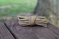 Coiled round shoelaces with metal aglets resting on a weathered wooden surface outdoors