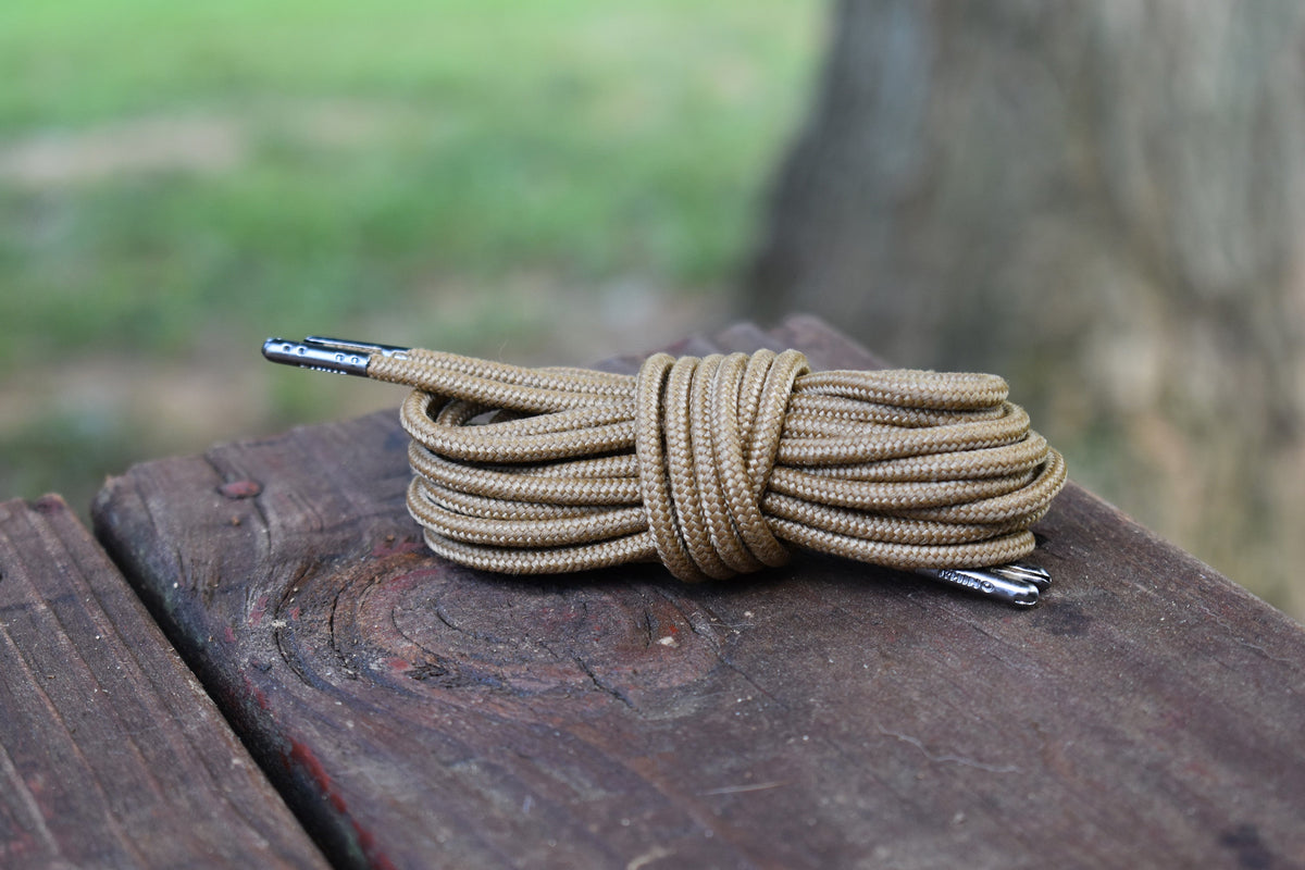 Coiled round shoelaces with metal aglets resting on a weathered wooden surface outdoors