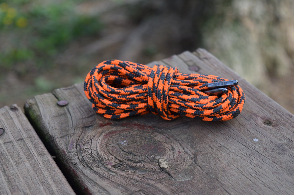 Coiled round shoelaces with orange and black speckled pattern resting on weathered wood