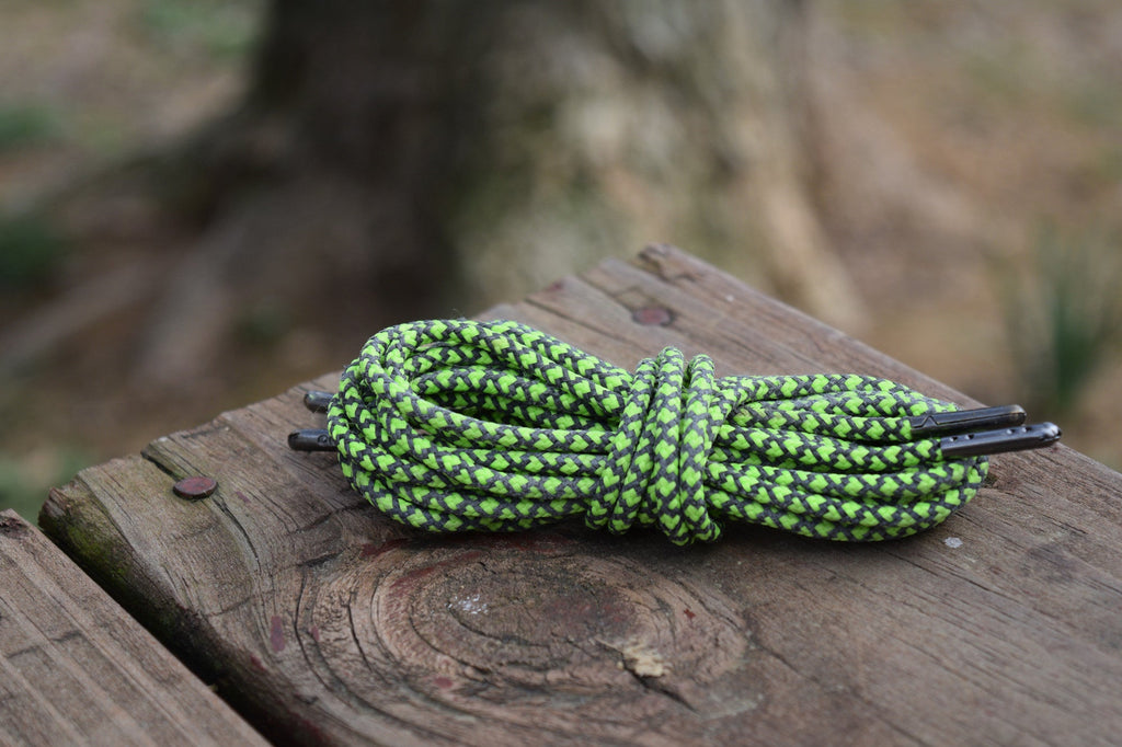 Round braided shoelaces in green and black pattern coiled on a wooden surface outdoors
