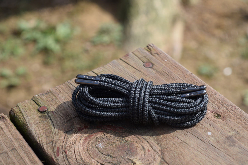 Coiled round black shoelaces with metal aglets resting on a weathered wooden surface outdoors