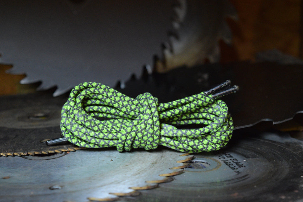 Green and black patterned round bootlaces coiled and knotted on a circular saw blade
