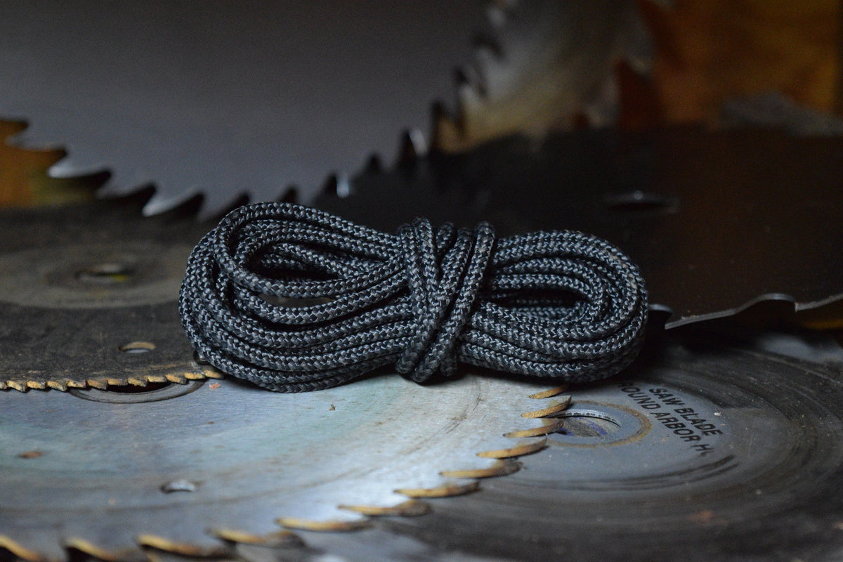 Coiled black braided paracord laces displayed on rustic circular saw blades