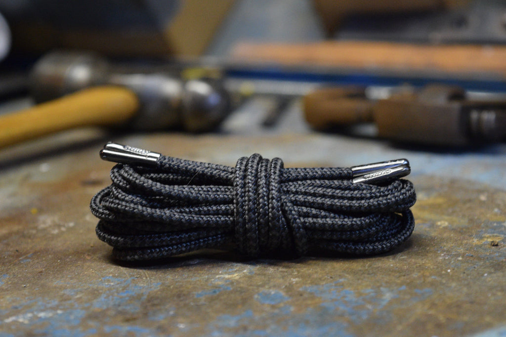 Coiled black round shoelaces with silver metal aglets resting on a worn metal surface