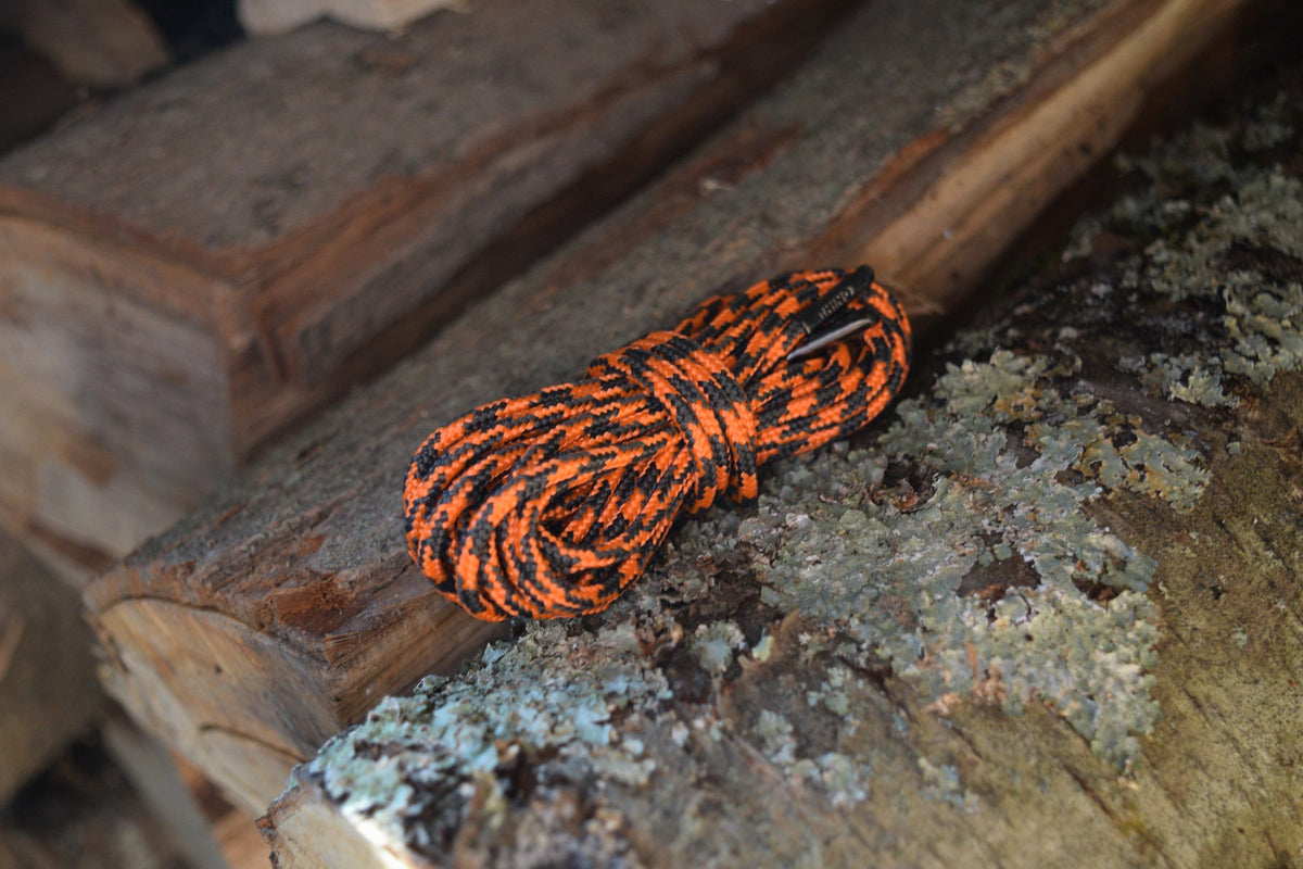 Coiled orange and black paracord shoelaces resting on a rustic log with lichen