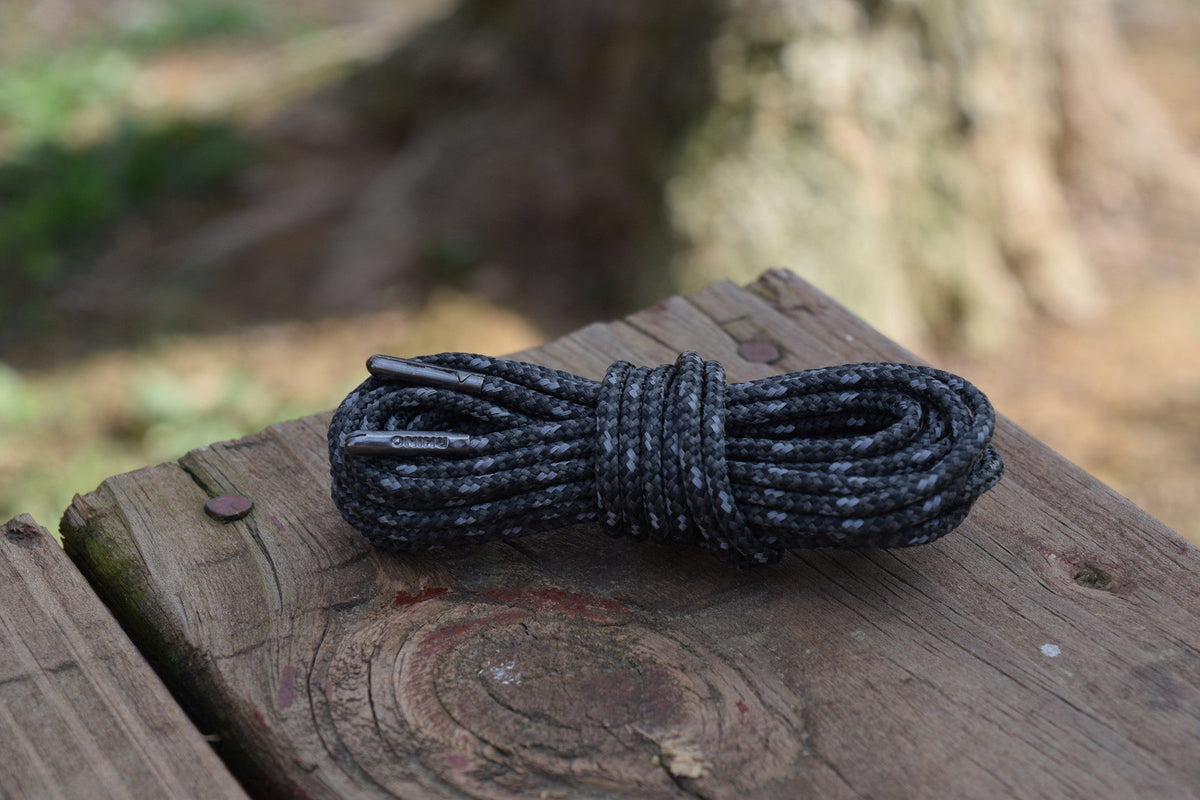 Coiled black and grey reflective round bootlaces resting on a weathered wooden surface outdoors