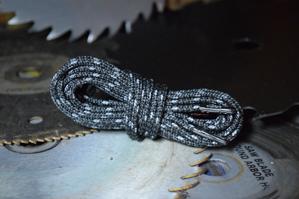 Coiled black and white reflective bootlaces with metal aglets resting on saw blades