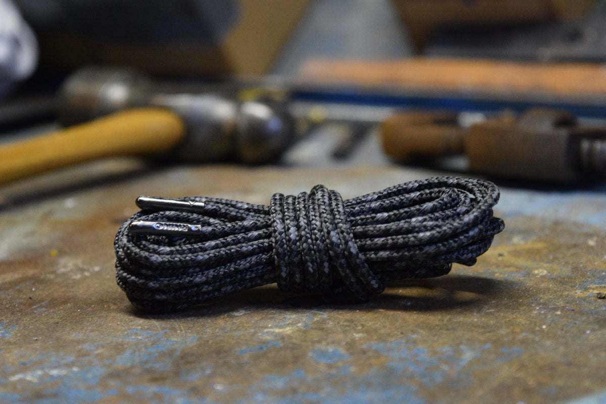 Coiled black reflective round shoelaces with metal aglets resting on a worn work surface