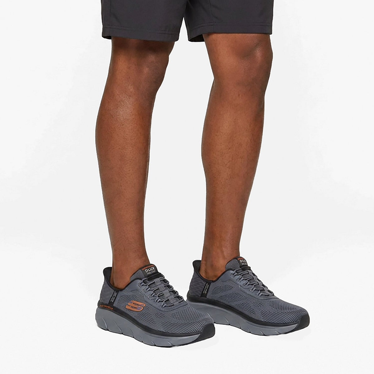Man wearing Skechers D'Lux Walker lace-up sneakers with dark shorts, on-foot lifestyle view