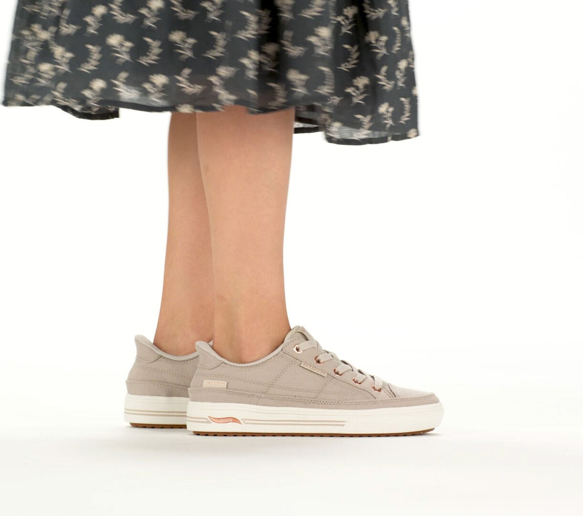 Woman wearing taupe low-top lace-up sneakers with white platform sole and floral midi skirt