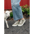 Woman wearing sage olive lace-up sneakers with side zipper, paired with cropped jeans near a lamb