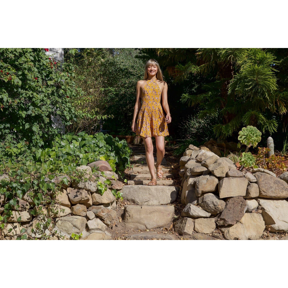 Woman wearing Taos Double U sandals walks down stone garden steps in sunlight