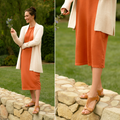 Woman wearing caramel T-strap sandals with orange dress on stone wall outdoors